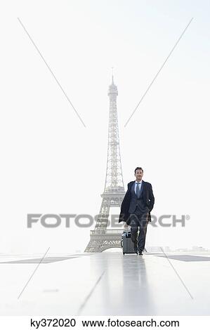 Stock Image - Businessman walking with luggage with the Eiffel Tower in the background, Paris, Ile-de-France, France. Fotosearch