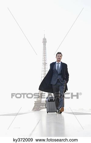 Stock Photo - Businessman walking with luggage with the Eiffel Tower in the background, Paris, Ile-de-France, France. Fotosearch
