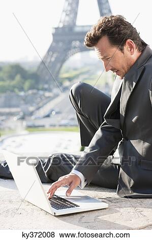 Stock Photo - Businessman working on a laptop with the Eiffel Tower in the background, Paris, Ile-de-France, France. Fotosearch