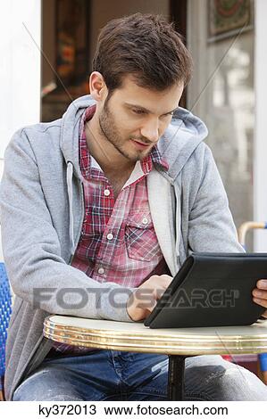 Man sitting at a sidewalk cafe using a digital tablet, Paris, Ile-de-France, France View Large Photo Image Stock Image - Man sitting at a sidewalk cafe using a digital tablet, Paris, Ile-de-France, France. Fotosearch