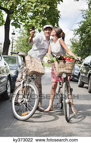 Stock Image - Couple riding bicycles and taking a picture of themselves with a mobile phone, Paris, Ile-de-France, France. Fotosearch