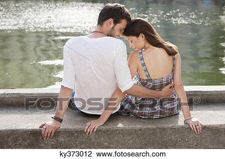 Rear view of a couple sitting at the ledge of a canal, Paris, Ile-de-France, France View Large Photo Image Stock Image - Rear view of a couple sitting at the ledge of a canal, Paris, Ile-de-France, France. Fotosearch