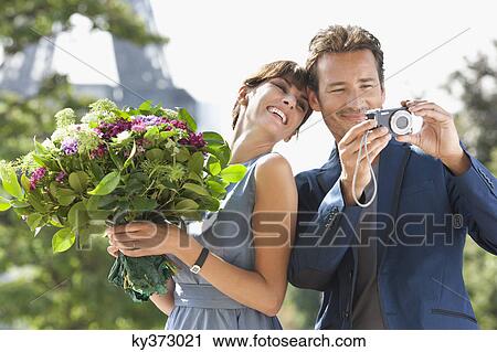 Woman holding a bouquet of flowers and man showing pictures in a digital camera with the Eiffel Tower in the background, Paris, Ile-de-France, France View Large Photo Image Stock Image - Woman holding a bouquet of flowers and man showing pictures in a digital camera with the Eiffel Tower in the background, Paris, Ile-de-France, France. Fotosearch