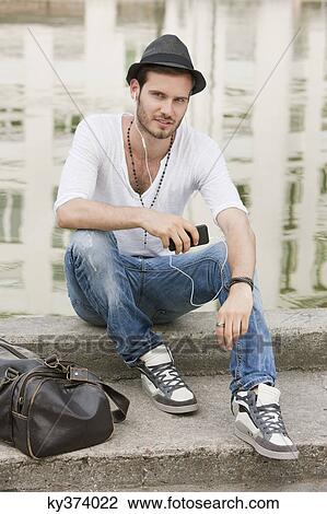Man sitting on the ledge of a canal and listening to music with an MP3 player, Paris, Ile-de-France, France View Large Photo Image Stock Image - Man sitting on the ledge of a canal and listening to music with an MP3 player, Paris, Ile-de-France, France. Fotosearch