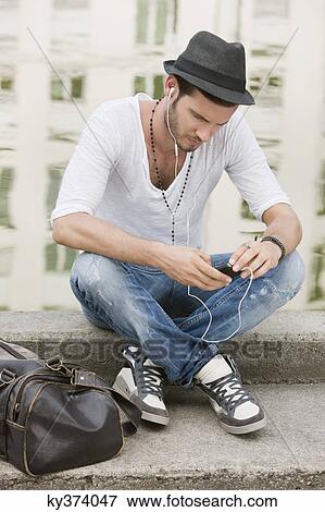 Man sitting on the ledge of a canal and listening to music with an MP3 player, Paris, Ile-de-France, France View Large Photo Image Stock Photo - Man sitting on the ledge of a canal and listening to music with an MP3 player, Paris, Ile-de-France, France. Fotosearch
