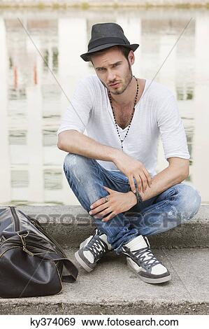 Stock Photo - Man sitting on the ledge of a canal, Paris, Ile-de-France, France. Fotosearch