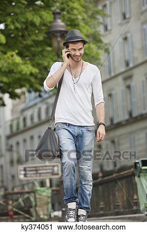Stock Image - Man walking on the road and talking on a mobile phone, Paris, Ile-de-France, France. Fotosearch