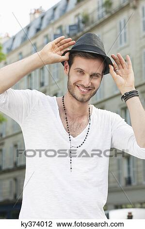 Stock Image - Portrait of a man adjusting his hat, Paris, Ile-de-France, France. Fotosearch