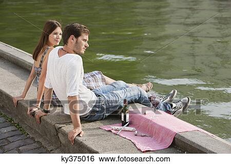 Couple sitting at the ledge of a canal, Paris, Ile-de-France, France View Large Photo Image Stock Photograph - Couple sitting at the ledge of a canal, Paris, Ile-de-France, France. Fotosearch