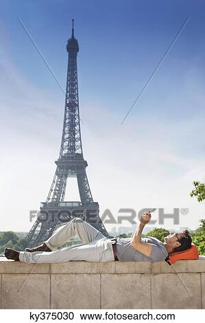 Man lying on a stone wall with the Eiffel Tower in the background, Paris, Ile-de-France, France View Large Photo Image Stock Image - Man lying on a stone wall with the Eiffel Tower in the background, Paris, Ile-de-France, France. Fotosearch
