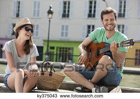 Stock Image - Man playing a guitar with a woman smiling, Canal St Martin, Paris, Ile-de-France, France. Fotosearch