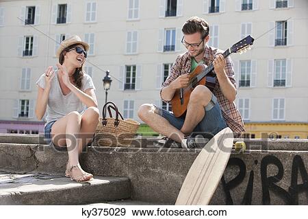 Stock Photo - Man playing a guitar with a woman clapping and smiling, Canal St Martin, Paris, Ile-de-France, France. Fotosearch