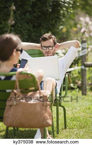 Stock Photo - Man sitting in a garden and looking at a laptop, Paris, Ile-de-France, France. Fotosearch