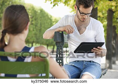 Man using a digital tablet with a woman sitting in front of him, Jardin des Tuileries, Paris, Ile-de-France, France View Large Photo Image Stock Photograph - Man using a digital tablet with a woman sitting in front of him, Jardin des Tuileries, Paris, Ile-de-France, France. Fotosearch