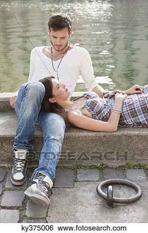 Stock Photograph - Woman lying on lap of a man at the ledge of a canal, Paris, Ile-de-France, France. Fotosearch