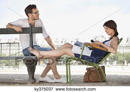 Stock Photo - Woman using a mobile phone with a man sitting in front of her, Jardin des Tuileries, Paris, Ile-de-France, France. Fotosearch