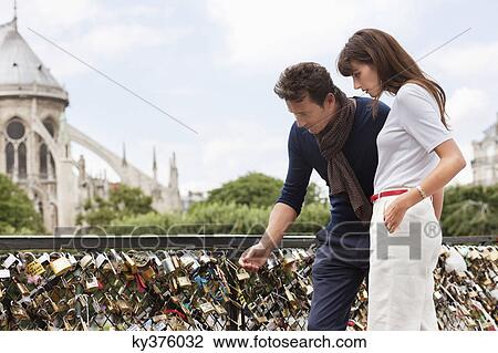Couple locking a padlock of love on a bridge, Pont des Arts, Notre Dame de Paris, Paris, Ile-de-France, France View Large Photo Image Stock Image - Couple locking a padlock of love on a bridge, Pont des Arts, Notre Dame de Paris, Paris, Ile-de-France, France. Fotosearch