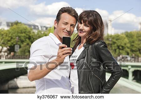 Stock Photo - Couple taking a picture of themselves with a mobile phone, Seine River, Paris, Ile-de-France, France. Fotosearch