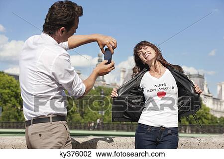 Stock Image - Man taking a picture of a woman with a mobile phone, Seine River, Paris, Ile-de-France, France. Fotosearch