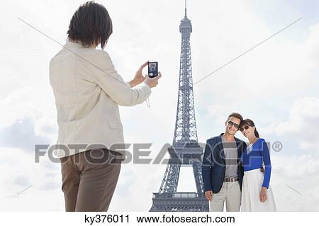 Stock Image - Woman taking a picture of couple with the Eiffel Tower in the background, Paris, Ile-de-France, France. Fotosearch