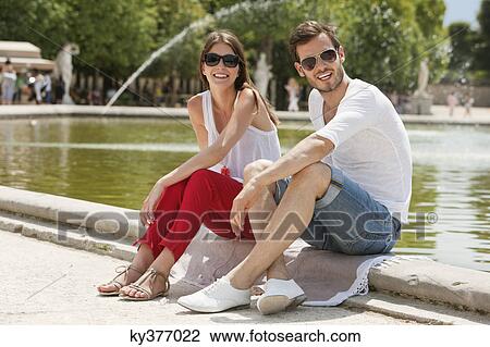 Stock Image - Couple sitting in a garden, Bassin octogonal, Jardin des Tuileries, Paris, Ile-de-France, France. Fotosearch