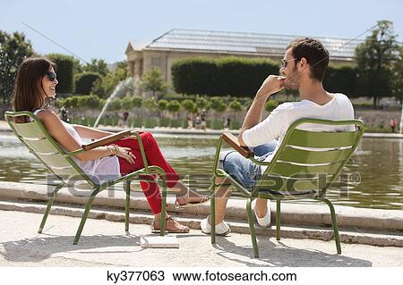 Stock Image - Couple sitting in chairs near a pond in a garden, Bassin octogonal, Jardin des Tuileries, Paris, Ile-de-France, France. Fotosearch