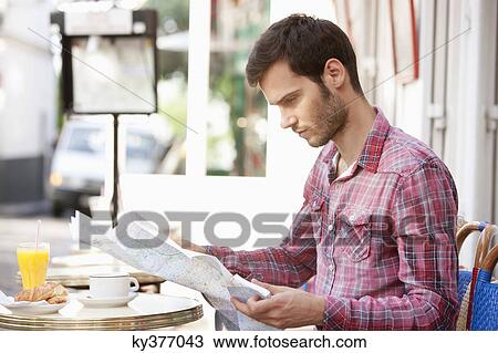 Stock Image - Man sitting at a sidewalk cafe and reading a map, Paris, Ile-de-France, France. Fotosearch