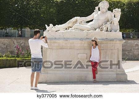 Man taking a picture of a woman standing near a sculpture in a garden, Jardin des Tuileries, Paris, Ile-de-France, France View Large Photo Image Stock Photography - Man taking a picture of a woman standing near a sculpture in a garden, Jardin des Tuileries, Paris, Ile-de-France, France. Fotosearch