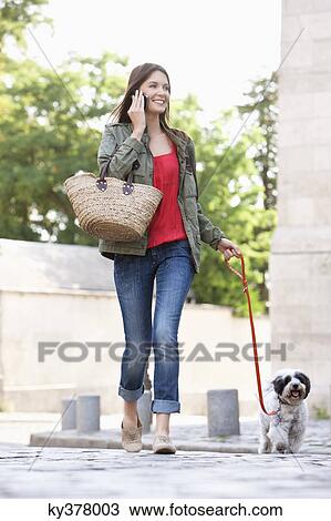 Stock Image - Woman holding a puppy on leash while talking on a mobile phone, Paris, Ile-de-France, France. Fotosearch