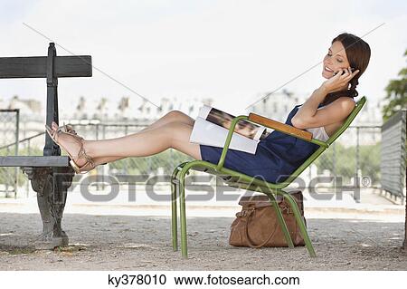 Stock Image - Woman reclining in a chair and talking on a mobile phone, Jardin des Tuileries, Paris, Ile-de-France, France. Fotosearch