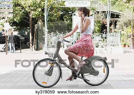 Stock Photo - Woman riding a bicycle and talking on a mobile phone, Paris, Ile-de-France, France. Fotosearch