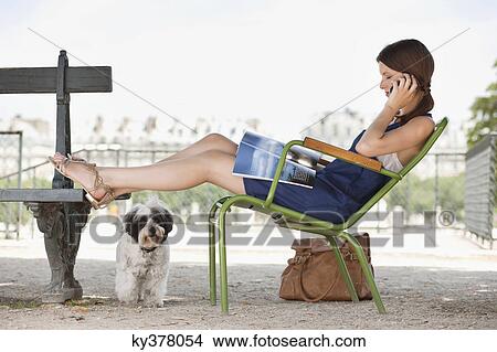 Woman sitting in a chair reading a magazine and talking on a mobile phone, Jardin des Tuileries, Paris, Ile-de-France, France View Large Photo Image Picture - Woman sitting in a chair reading a magazine and talking on a mobile phone, Jardin des Tuileries, Paris, Ile-de-France, France. Fotosearch