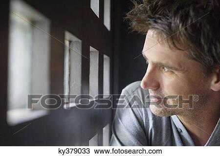 Stock Image - Close-up of a man looking through small windows. Fotosearch