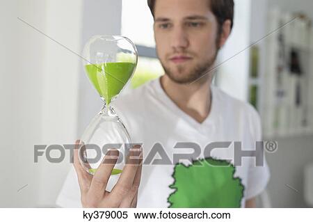 Man looking at an hourglass with green sand in it View Large Photo Image Stock Photography - Man looking at an hourglass with green sand in it. Fotosearch