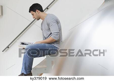 Stock Photo - Man sitting on stairs and reading a magazine. Fotosearch