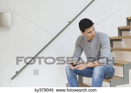 Man sitting on stairs using a mobile phone View Large Photo Image Stock Photography - Man sitting on stairs using a mobile phone. Fotosearch