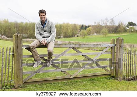 Man sitting on the gate of a cottage View Large Photo Image Stock Photo - Man sitting on the gate of a cottage. Fotosearch