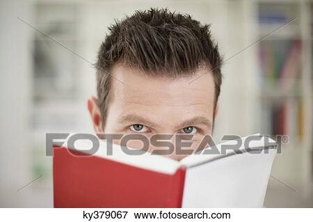 Stock Photo - Portrait of a man holding a book in front of his face. Fotosearch