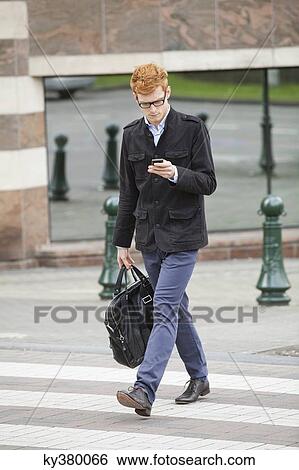 Businessman crossing a road while using a mobile phone View Large Photo Image Stock Photograph - Businessman crossing a road while using a mobile phone. Fotosearch