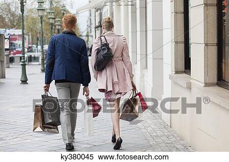 Rear view of a couple carrying shopping bags View Large Photo Image Stock Photography - Rear view of a couple carrying shopping bags. Fotosearch