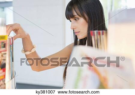 Close-up of a woman choosing magazine from a bookshelf View Large Photo Image Stock Photo - Close-up of a woman choosing magazine from a bookshelf. Fotosearch