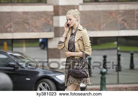 Stock Image - Woman crossing the road while talking on a mobile phone. Fotosearch
