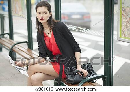 Woman sitting at a bus stop and holding a newspaper View Large Photo Image Stock Photograph - Woman sitting at a bus stop and holding a newspaper. Fotosearch