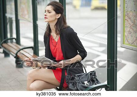 Woman sitting at a bus stop and holding a newspaper View Large Photo Image Stock Photography - Woman sitting at a bus stop and holding a newspaper. Fotosearch