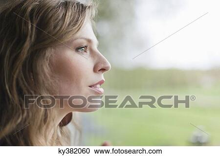 Stock Image - Close-up of a woman looking through window. Fotosearch