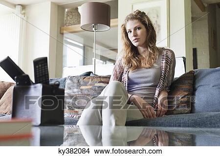 Picture - Portrait of a beautiful woman sitting on a couch at home. Fotosearch