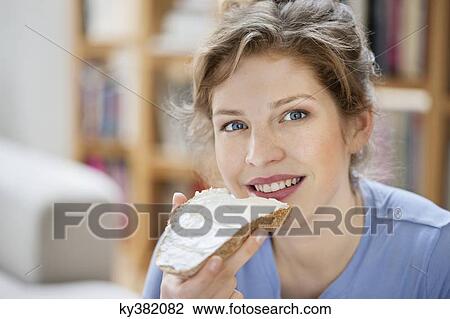 Stock Image - Portrait of a woman eating toast with cream spread on it. Fotosearch