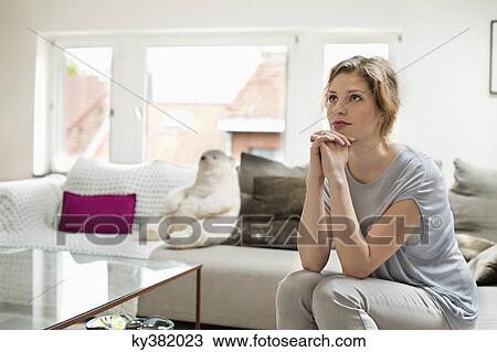Stock Image - Woman sitting on a couch and looking away. Fotosearch