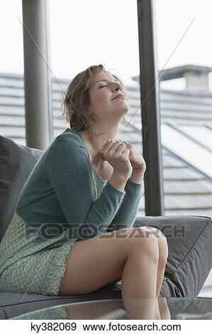 Stock Photo - Woman sitting on a couch with her eyes closed. Fotosearch