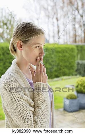 Stock Image - Woman smoking cigarette in park. Fotosearch